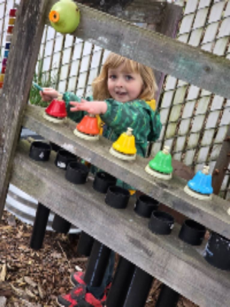 Child exploring colorful bells in the outdoor music area