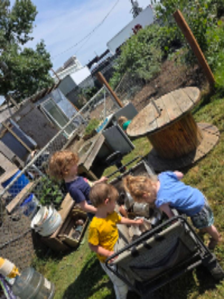 Children working together to move the outdoor mud kitchen